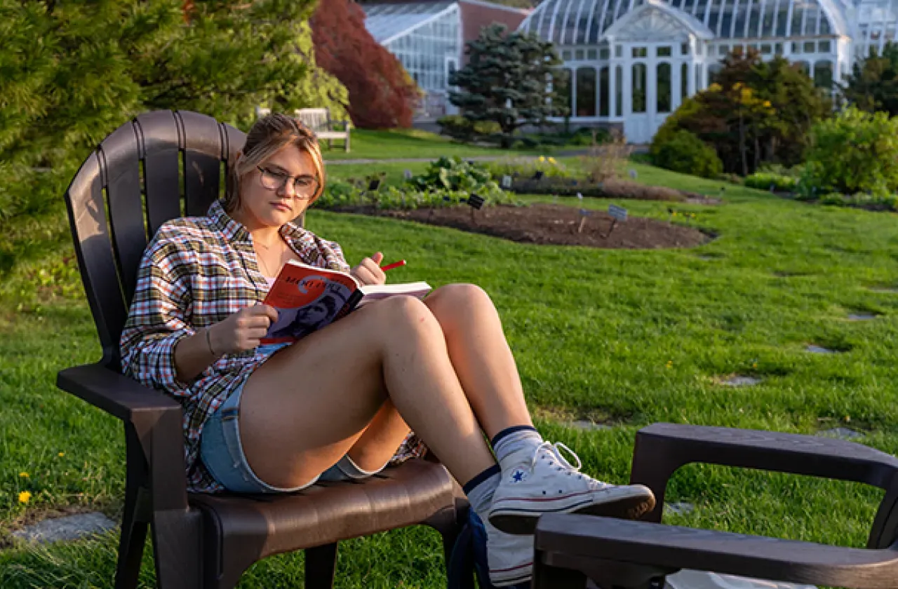 学生坐在莱曼植物屋前的椅子上，看一本书.
